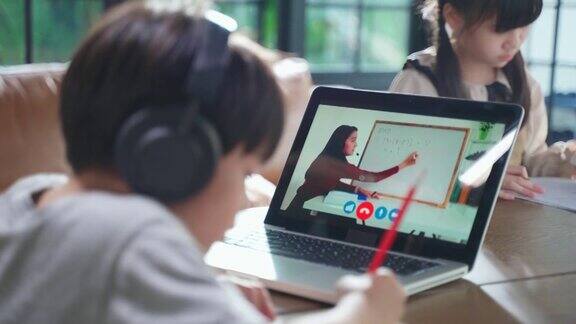由于冠状病毒大流行亚洲小男孩通过数字远程互联网会议从学校老师那里学习在线课程孩子看着电脑笔记本电脑屏幕那个女人在教书