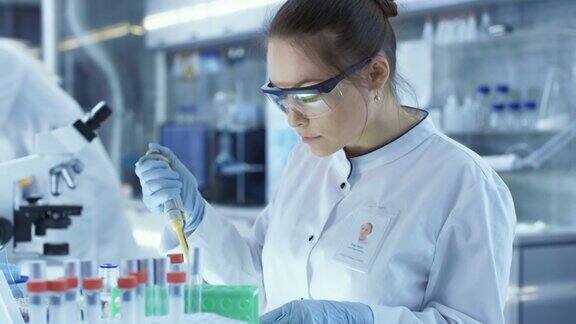 女研究科学家在一个大的现代实验室使用微型管填充试管在背景中科学家正在工作
