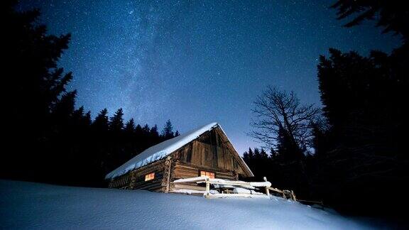 延时美丽的木屋在冬天的森林里在星空下