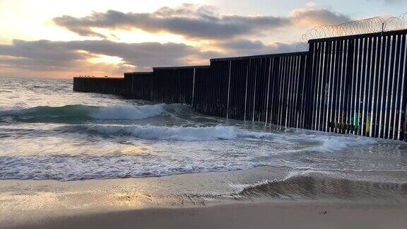 海滩和海浪的近景日落附近的国际边界墙在PlayasTijuana墨西哥