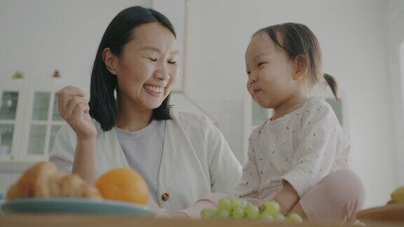 快乐的亚洲妇女和小女儿在厨房里玩用健康的食物喂孩子