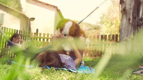 年轻快乐的小女孩在夏令营躺在彩色的吊床上放松地玩在外面的毛绒狗娃娃在绿色的草地上孩子们孩子们的慢动作