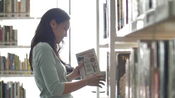 亚洲妇女在图书馆的书架上寻找和阅读一本书