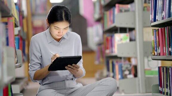 亚洲大学图书馆一名亚洲女子正在图书馆用平板电脑上网