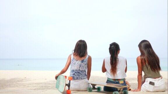 一群快乐的亚洲女性朋友在玩完滑板后坐在沙滩上聊天