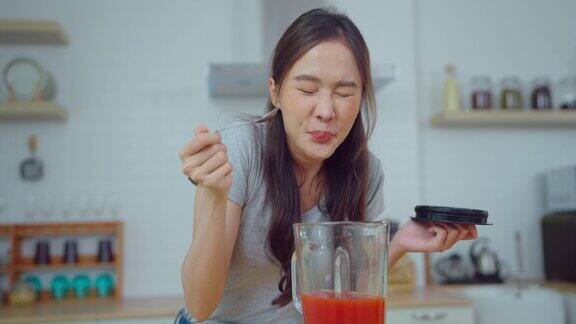 年轻的亚洲女人在家里的厨房里制作冰沙饮料她在家里笑着喝着饮料