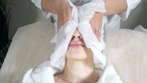 用无菌餐巾纸擦拭面部年轻漂亮的女人正在美容院接受治疗洁面泡沫使用