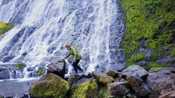 女人爬过瀑布脚下的岩石