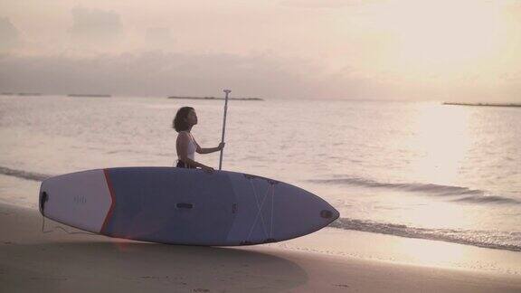 年轻女子准备一个早晨的冲浪享受在海滩上的活力在太阳升起