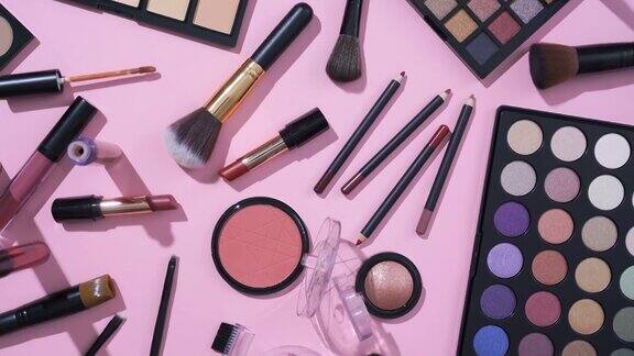 在粉红色的背景上旋转化妆品和化妆笔刷集合