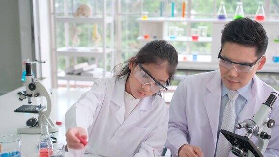 在实验室老师教年轻的科学家女孩学习用滴管或短吸管在烧瓶或烧杯中混合彩色液体