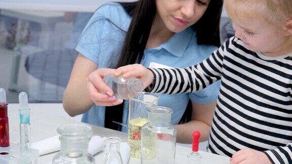 年轻女子在试管中混合液体多民族儿童观看学习科学化学亚洲学校的老师和学生在科学课上