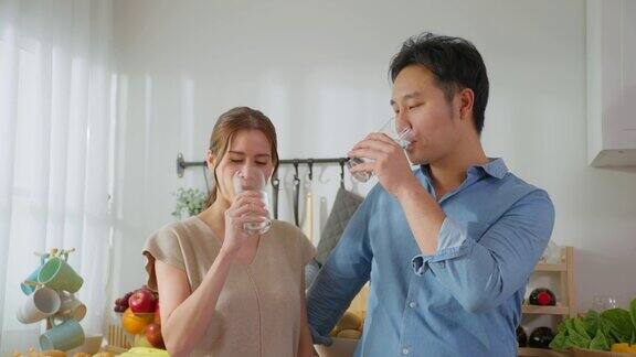 亚洲美女夫妇在家里的厨房里喝一杯水年轻的口渴的男人和女人抱着干净的天然矿物在杯子醒来后在早上的卫生保健在家里啜饮