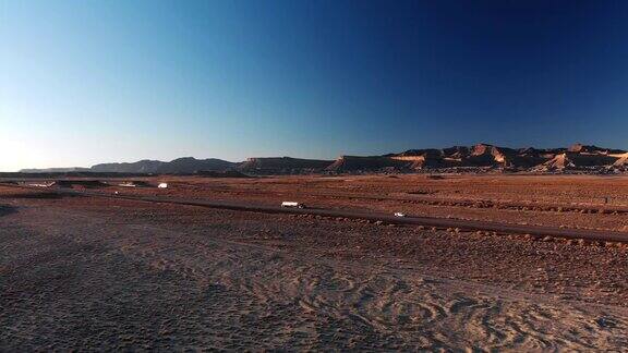 移动无人机在犹他州15号州际公路旁边的沙漠平原拍摄在日落日出时在晴朗的蓝天下有山脉作为背景