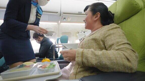 亚洲资深女商人获得空中小姐服务带防护口罩预防疾病为商务旅行提供美味的食物、茶