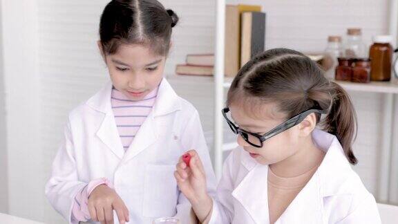 穿着白色长裙的可爱的小学女生在记事本上专心地做实验和记录现代技术教育孩子们在实验室的实验课上用玻璃管学习化学液体测试