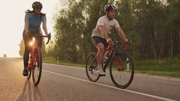 夕阳西下一男一女骑着自行车在路上慢动作地骑行这对夫妇骑自行车旅行运动自行车头盔