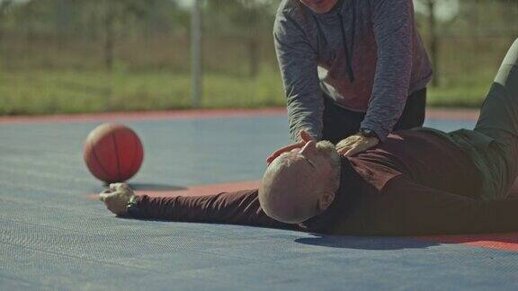 一名男子在篮球场上对一名心脏病发作的老人进行急救