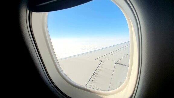 透过飞机的窗户观看飞机的机翼映衬着蓝天白云背景