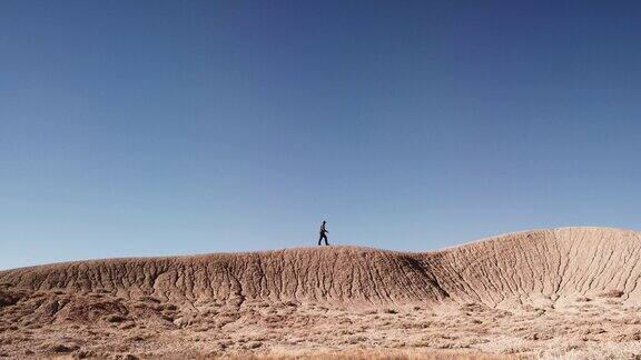 一个人爬上和走在一条条纹和侵蚀的沙漠山脊独自面对一个充满活力的蓝天