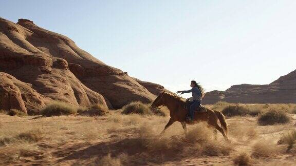 在一个阳光明媚的下午一个十几岁的美国土著女孩(纳瓦霍人)骑着她的马飞驰在亚利桑那州犹他州的纪念碑谷沙漠中的慢动作镜头