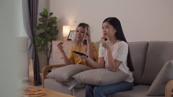 两个美女朋友在家里的客厅里一边看电视一边吃披萨