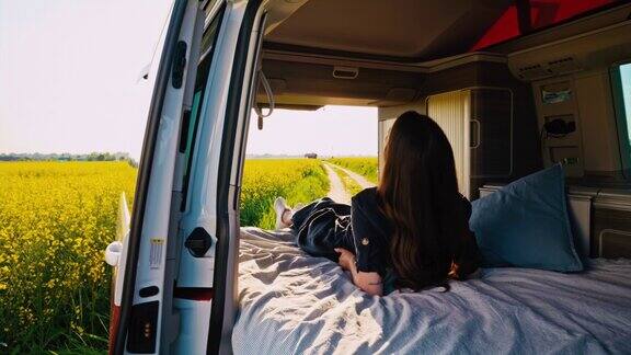 DS一名年轻女子躺在一辆露营车的小屋里车停在油菜籽田旁