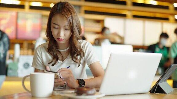 年轻的成年人快乐微笑的亚洲学生在线学习在网上聊天在网上聊天会议使用笔记本电脑在咖啡馆或办公室大学学院女生远程学习