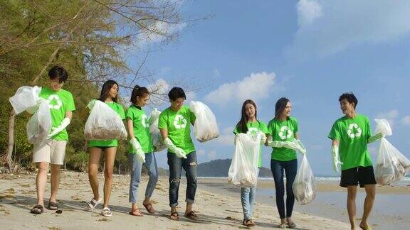 一群年轻的亚洲人志愿者穿着绿色t恤用装满垃圾的塑料袋清理海滩生态安全概念4k决议