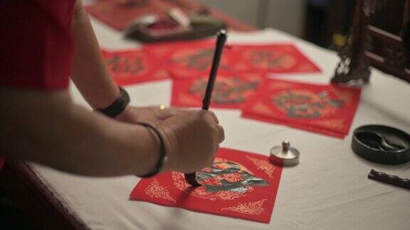 亚洲华人男性练习书法的手为即将到来的中国新年庆祝家庭装饰目的繁荣和良好的措词写在一张红色的纸上