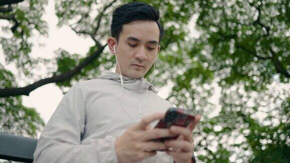 年轻的亚洲运动员在公园里使用智能手机