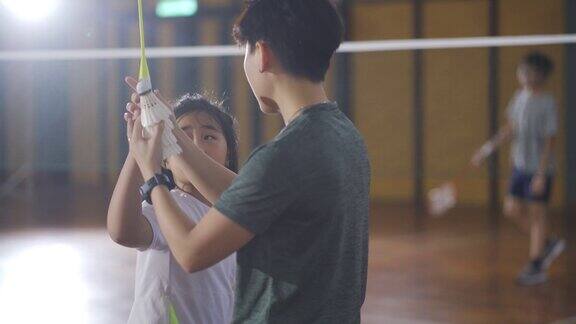 亚洲华人女羽毛球教练在羽毛球场上教她的学生