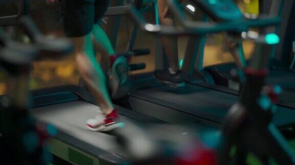 后视图低段男子的腿在健身房跑步机一起在晚上面对城市街灯