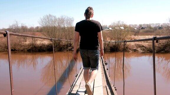 这个年轻人正走在河上的一座悬空木桥上后视图