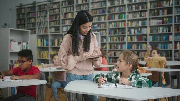 亚洲老师在学校图书馆帮助学生完成任务