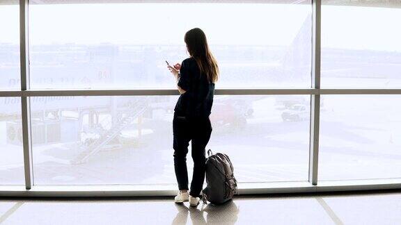 一个小女孩在机场窗边自拍快乐的背包欧洲游客在终端使用智能手机4k