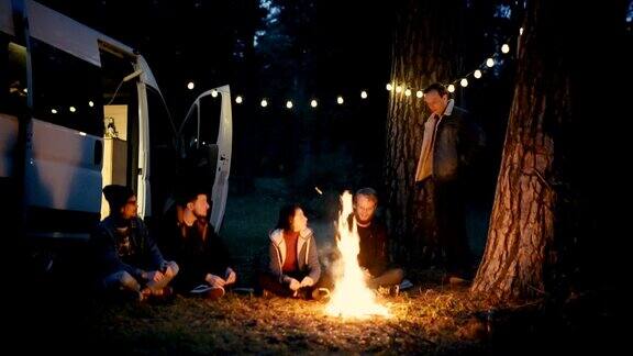 朋友们坐在森林里靠近露营车的篝火旁