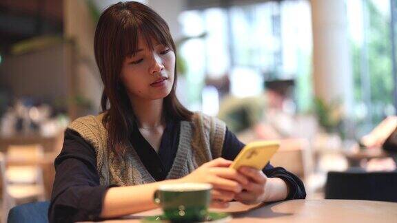一名亚洲女性在咖啡店一边喝咖啡一边看手机