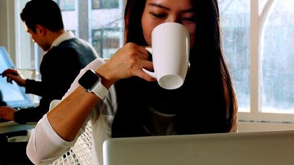 女性高管一边喝咖啡一边使用笔记本电脑