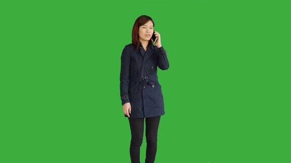 穿着蓝色外套的年轻亚洲女人使用智能手机数字平板电脑和看相机一个站在绿屏前的女人