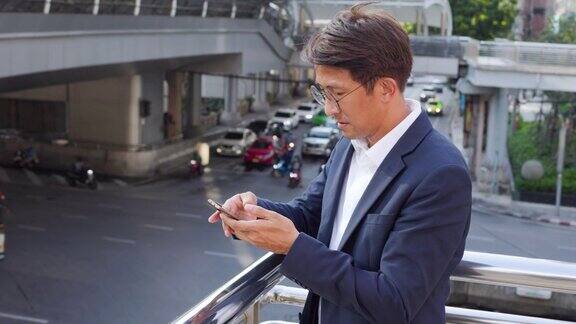 亚洲商人在办公大楼外用手机应用发短信