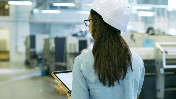 戴安全帽的美丽女工业工程师在大工厂里使用平板电脑