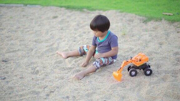 一个小男孩独自在操场上玩着挖土机玩具