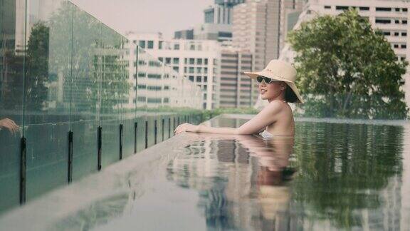 微笑的亚洲女性戴着帽子和太阳镜呆在酒店的游泳池里