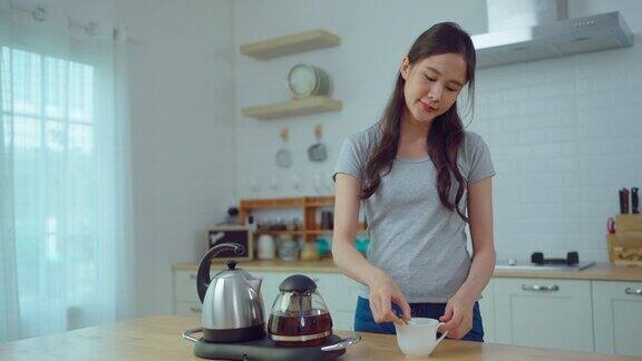 年轻的亚洲妇女在家里的厨房里煮茶或咖啡