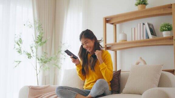 快乐的年轻亚洲女性在家里舒适的沙发上放松用智能手机发短信