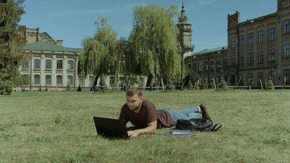 聪明的男学生在校园草坪上用笔记本电脑工作