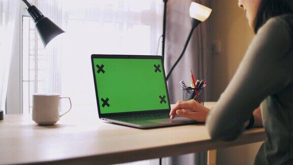女:在家里的桌子上使用绿色屏幕的笔记本电脑