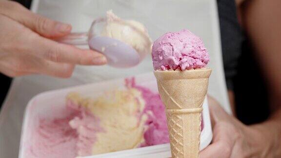 一个女人把第二勺冰淇淋放在粉色的华夫蛋筒上特写镜头