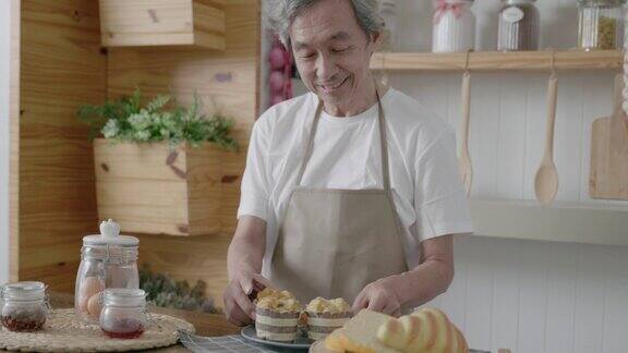 厨房里亚洲爷爷拿着盘子里的美味蛋糕对着镜头开心地微笑